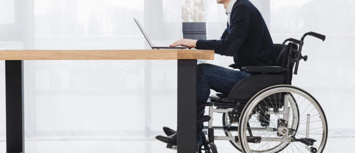side-view-young-businessman-sitting-wheelchair-using-laptop-new-office
